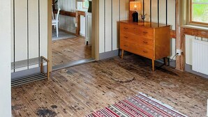 Una habitación con paneles de madera, un aparador de madera, un radiador y una ventana con vistas a la vegetación.