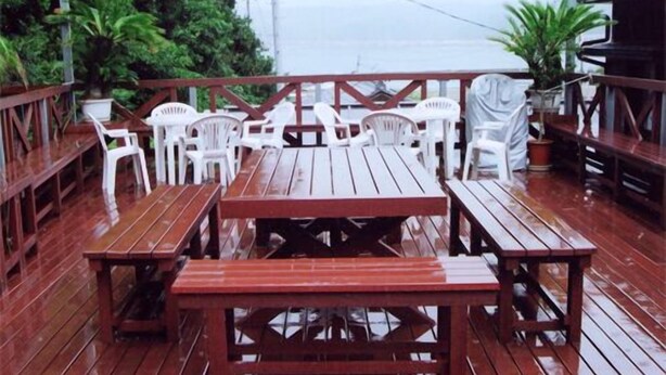 Una terraza de madera con mesas de picnic y sillas de plástico blancas.