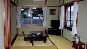 Una habitación japonesa tradicional con suelo de tatami, una mesa baja, un televisor y una ventana con cortinas.