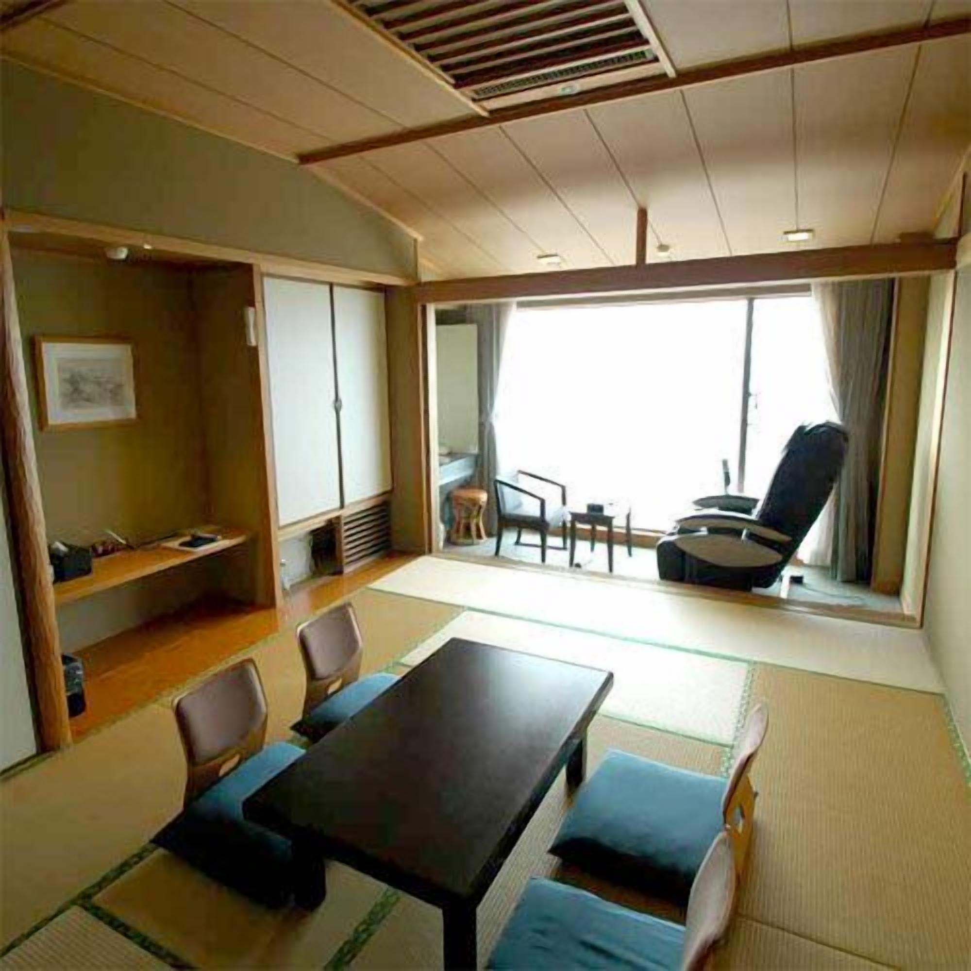 A room with a tatami mat floor, a table with chairs, a sofa, a window with curtains, and a small seating area with a chair and a table.