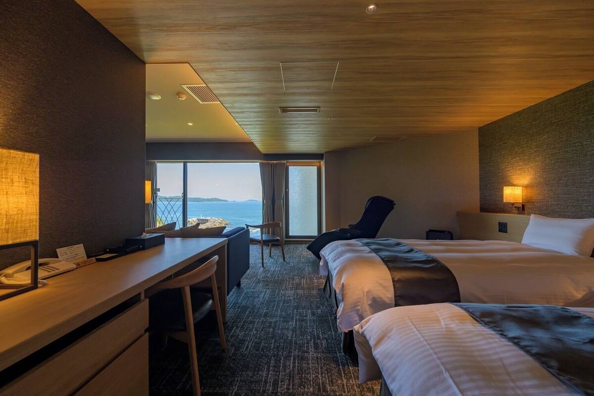 Habitación de hotel con escritorio, dos camas, una silla, vista al mar y techo de madera.
