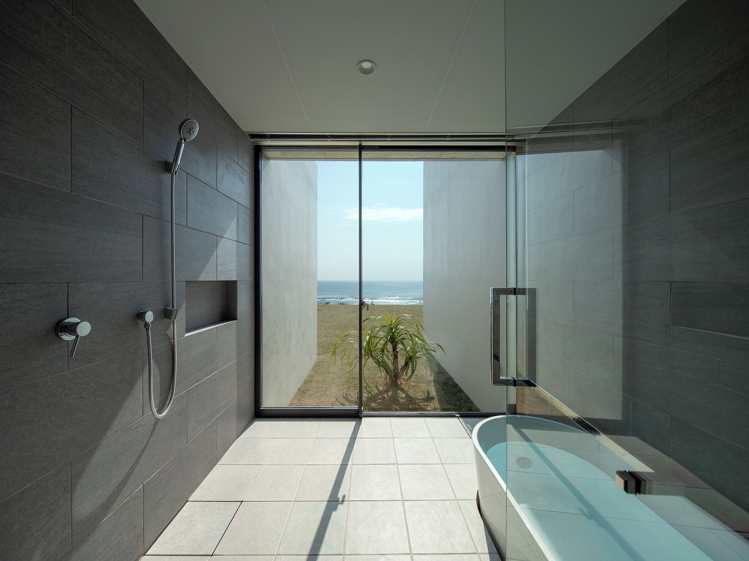 Un baño moderno con una puerta de cristal que da a un balcón con vistas al océano.
