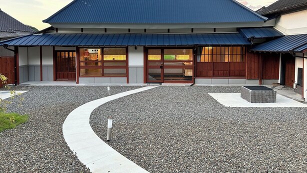 Un bâtiment traditionnel japonais avec un toit bleu, des portes coulissantes en bois et une cour recouverte de gravier.