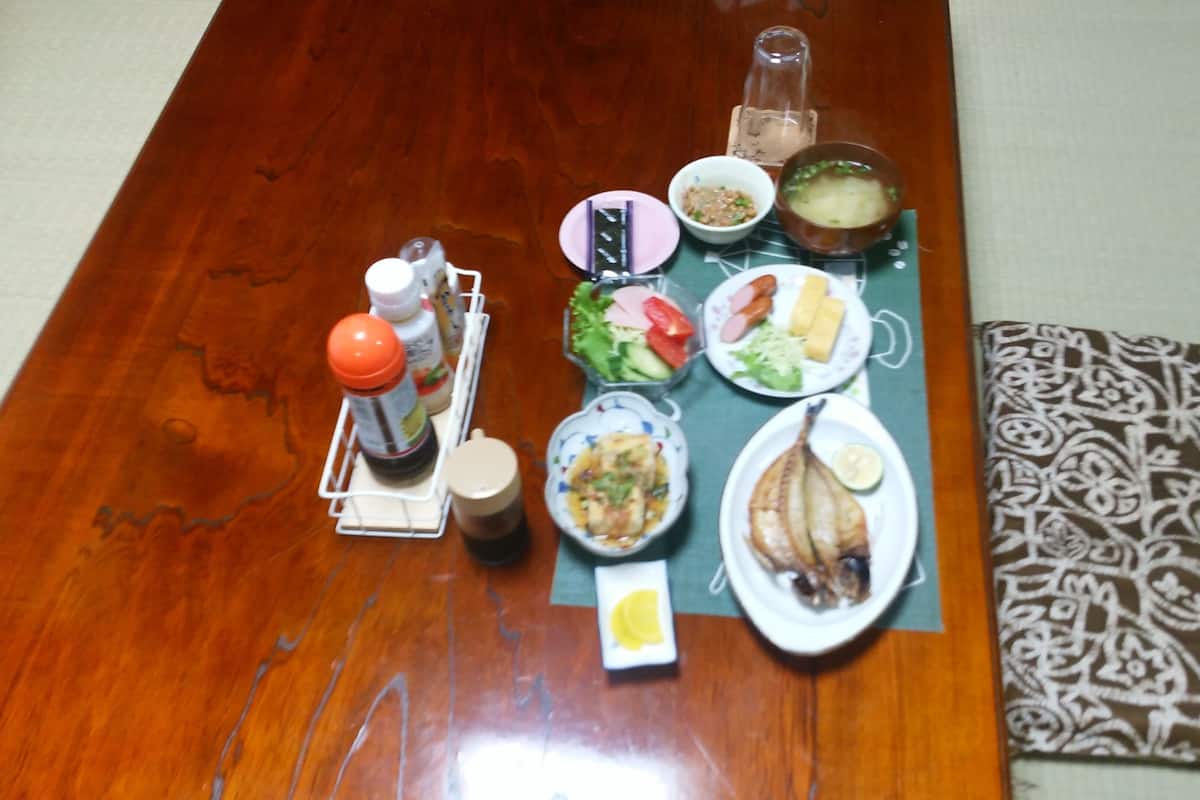 A wooden dining table with various dishes, condiments, and a bottle of water.