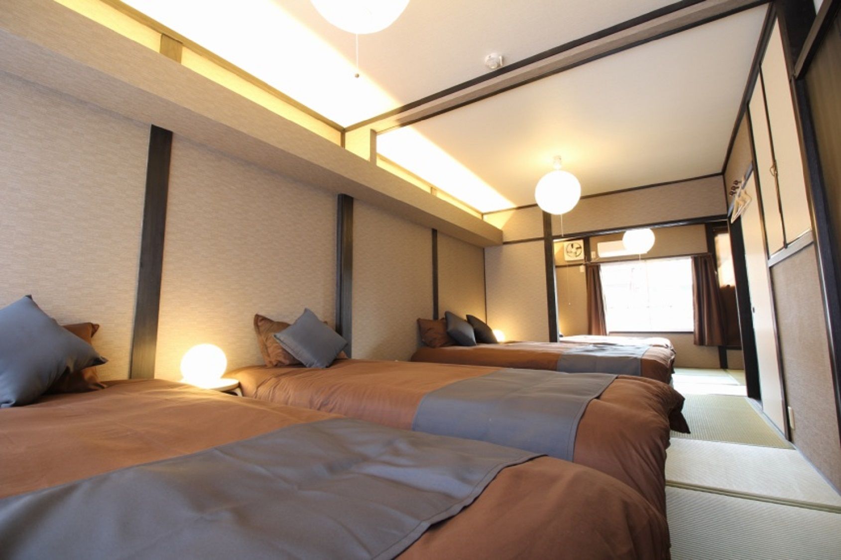 A hotel room with a large bed, a smaller bed, and a sofa. There are multiple pillows and a bedside table.