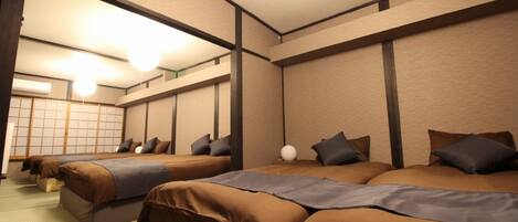 Ein Hotelzimmer mit mehreren nebeneinander liegenden Betten, einem traditionellen Tatami-Boden und einer Schiebetür zu einem traditionellen japanischen Raum.