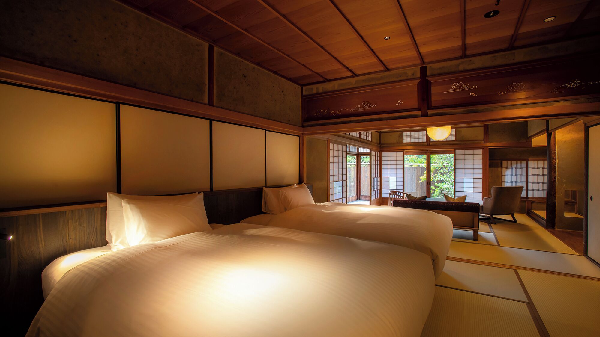 A traditional Japanese-style bedroom with tatami flooring, a large bed with white bedding, sliding shoji doors, and a view of greenery outside.