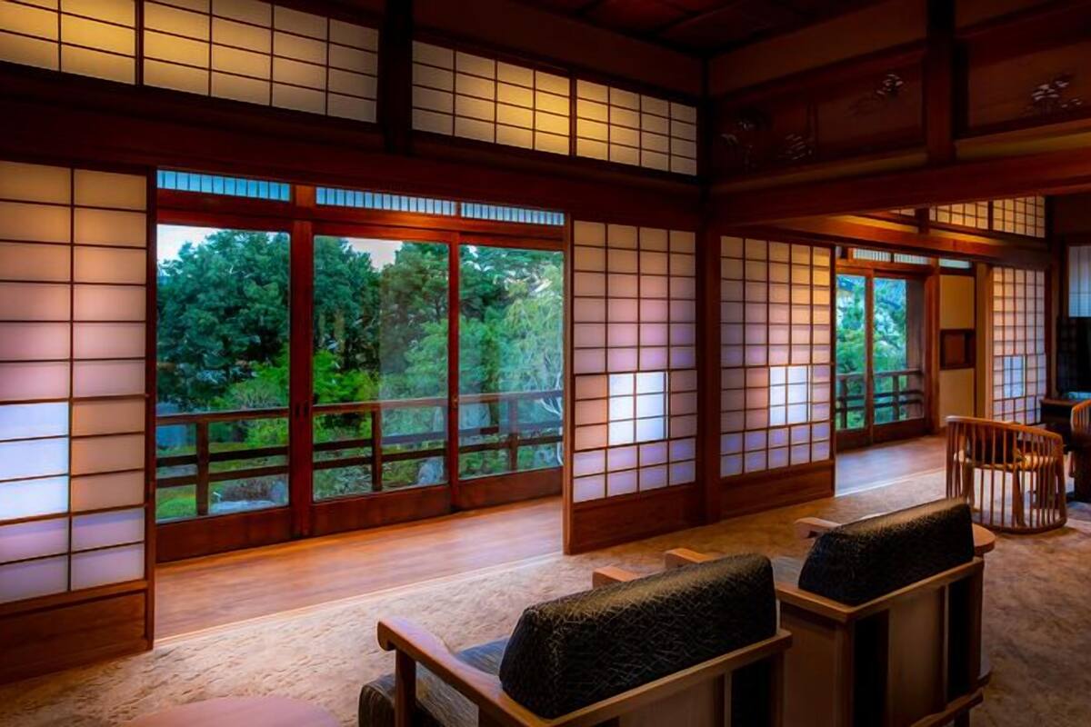 A traditional Japanese room with tatami flooring, sliding doors, and a view of greenery outside.