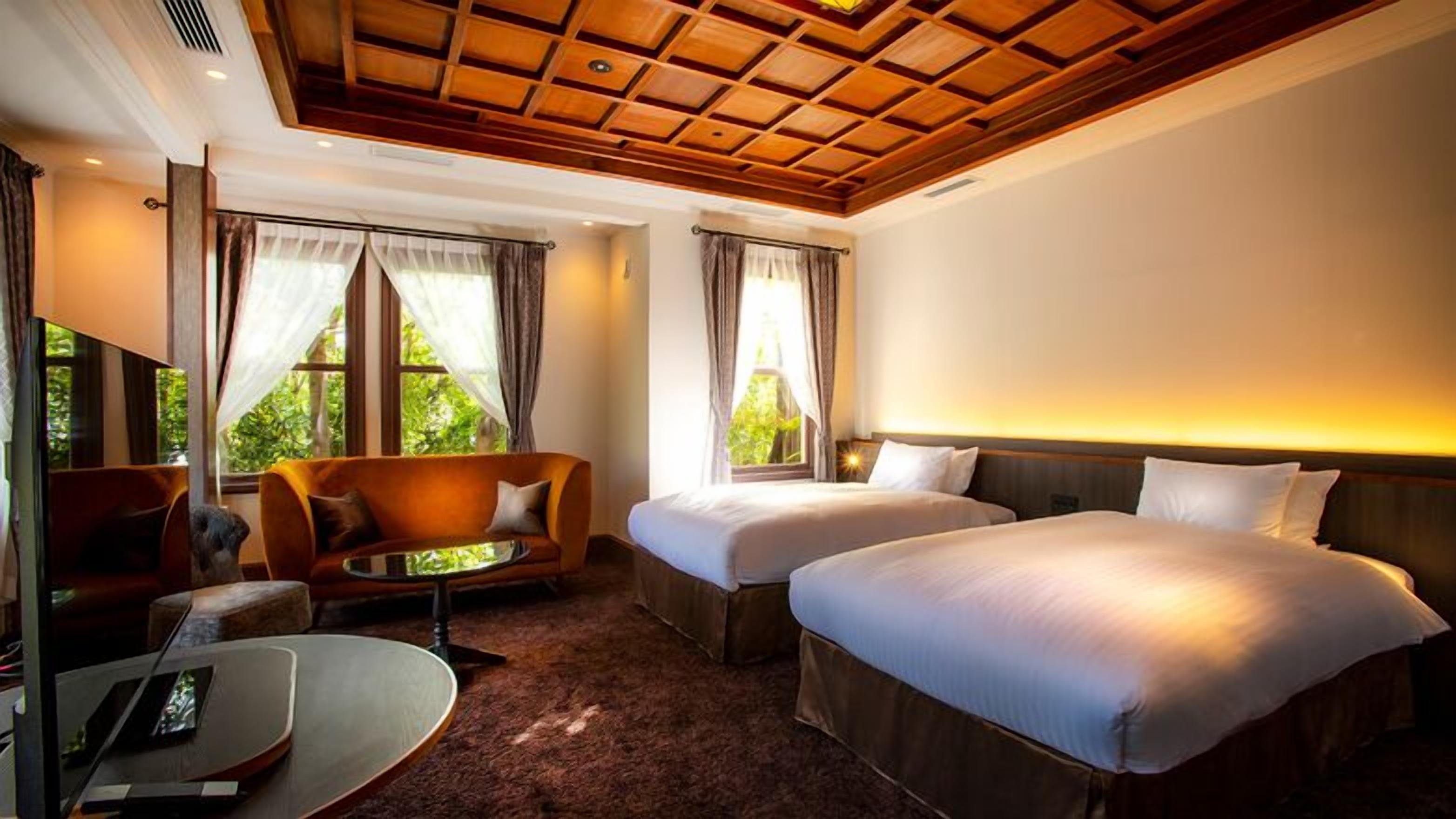 Habitación de hotel con dos camas, un sofá, un televisor y ventanas amplias.