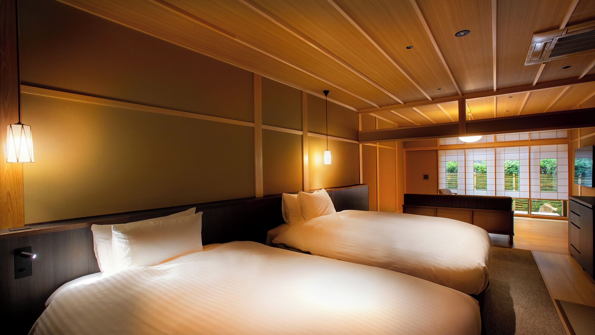 A hotel room with two beds, wooden ceiling, and large windows with a view of greenery.