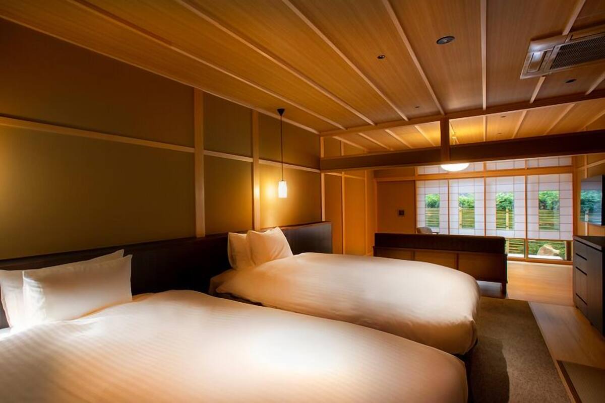A hotel room with two beds, wooden paneling, a view of greenery, and a traditional Japanese sliding door.