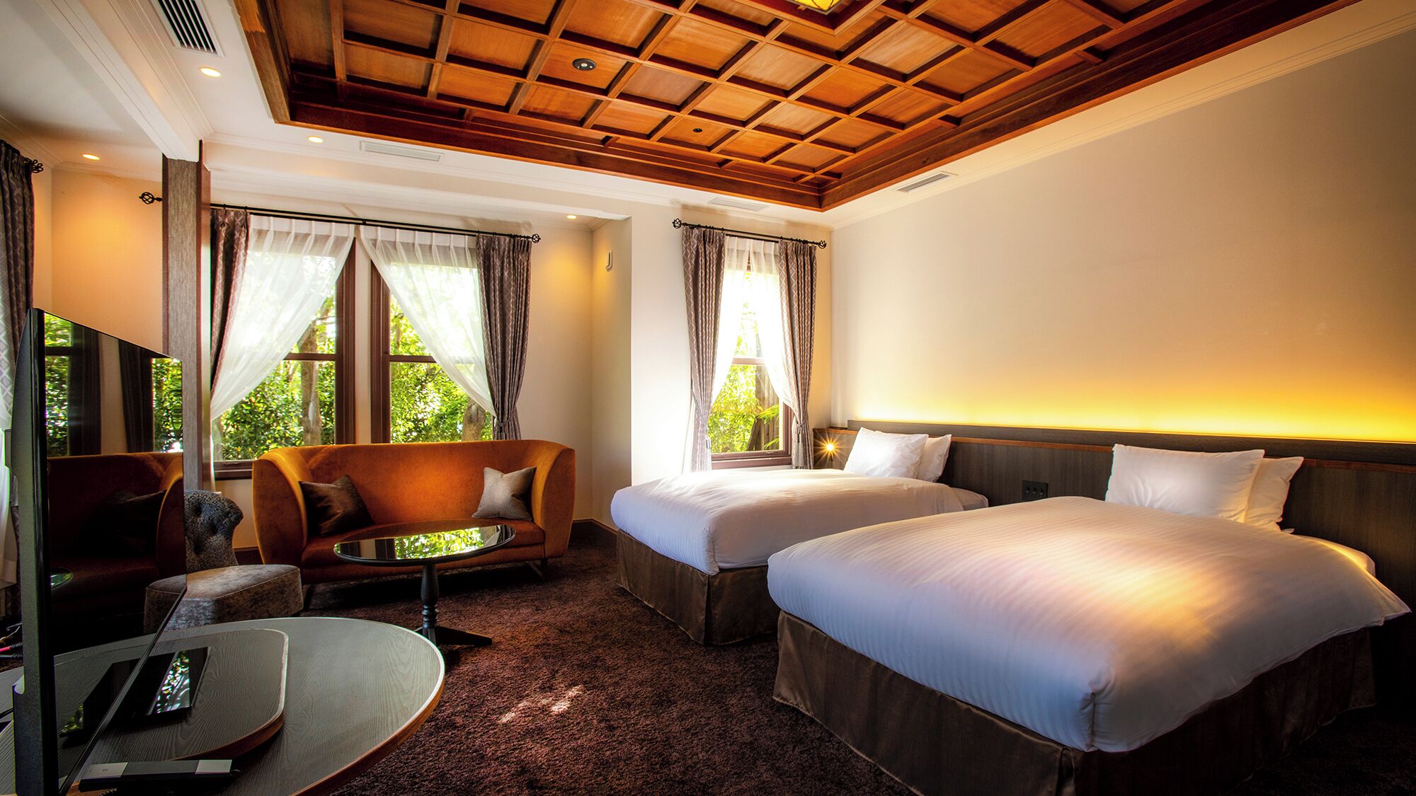A hotel room with two beds, a sofa, a TV, and a window with curtains.