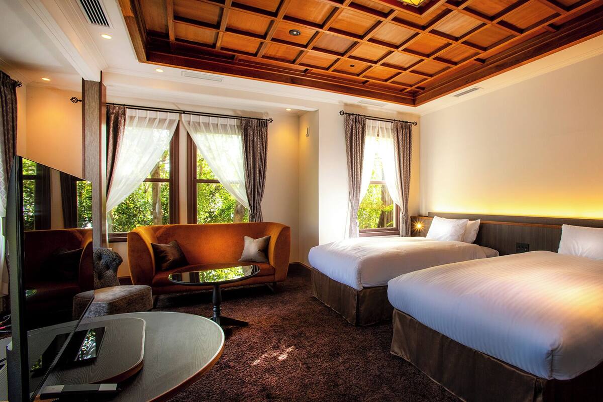 A hotel room with two beds, a sofa, a TV, and a window with curtains.