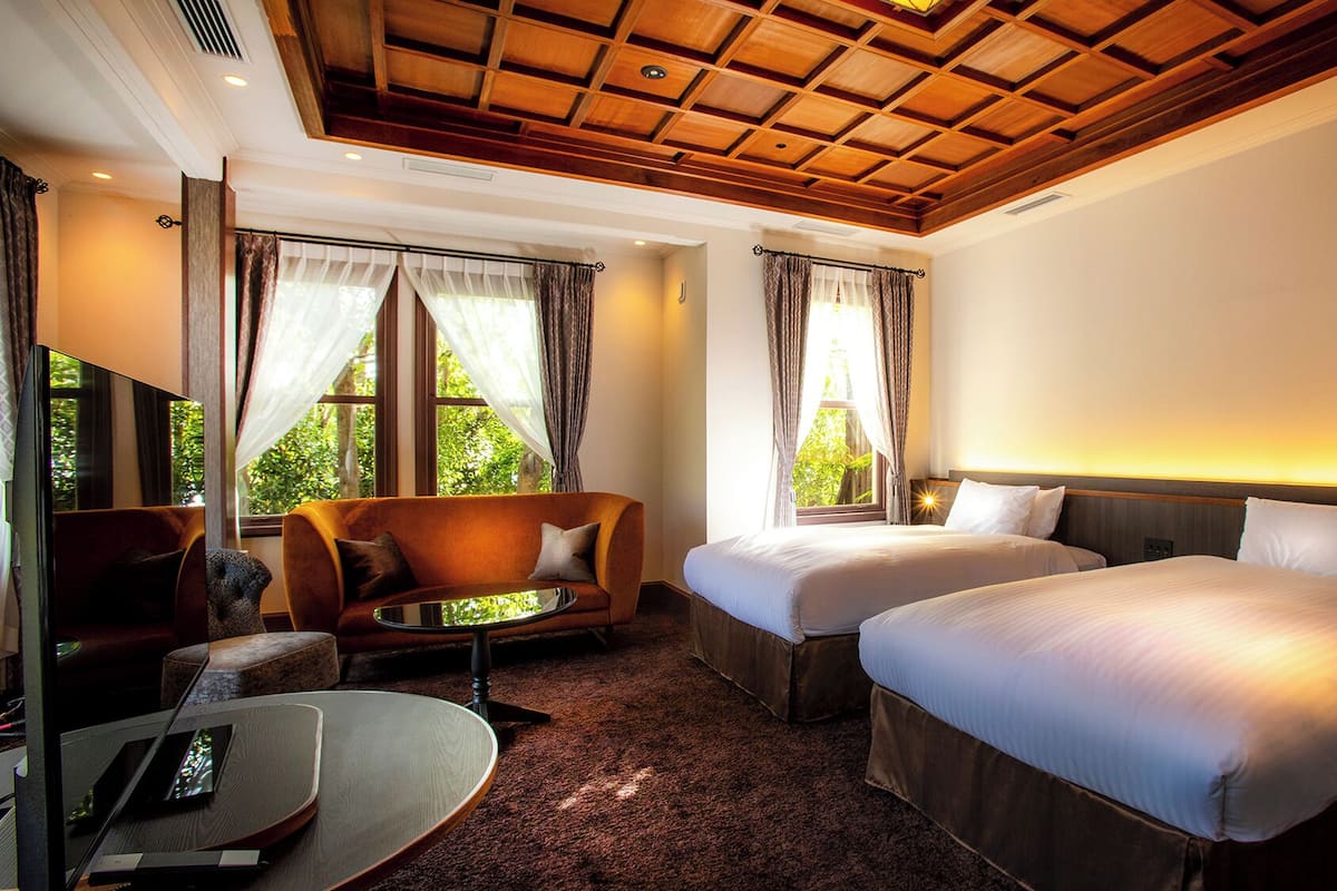 Habitación de hotel con dos camas, un sofá, un televisor y una ventana con cortinas.