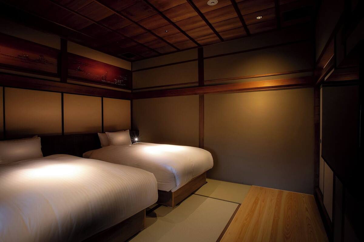 A room with two beds, wooden paneling, and a ceiling light.