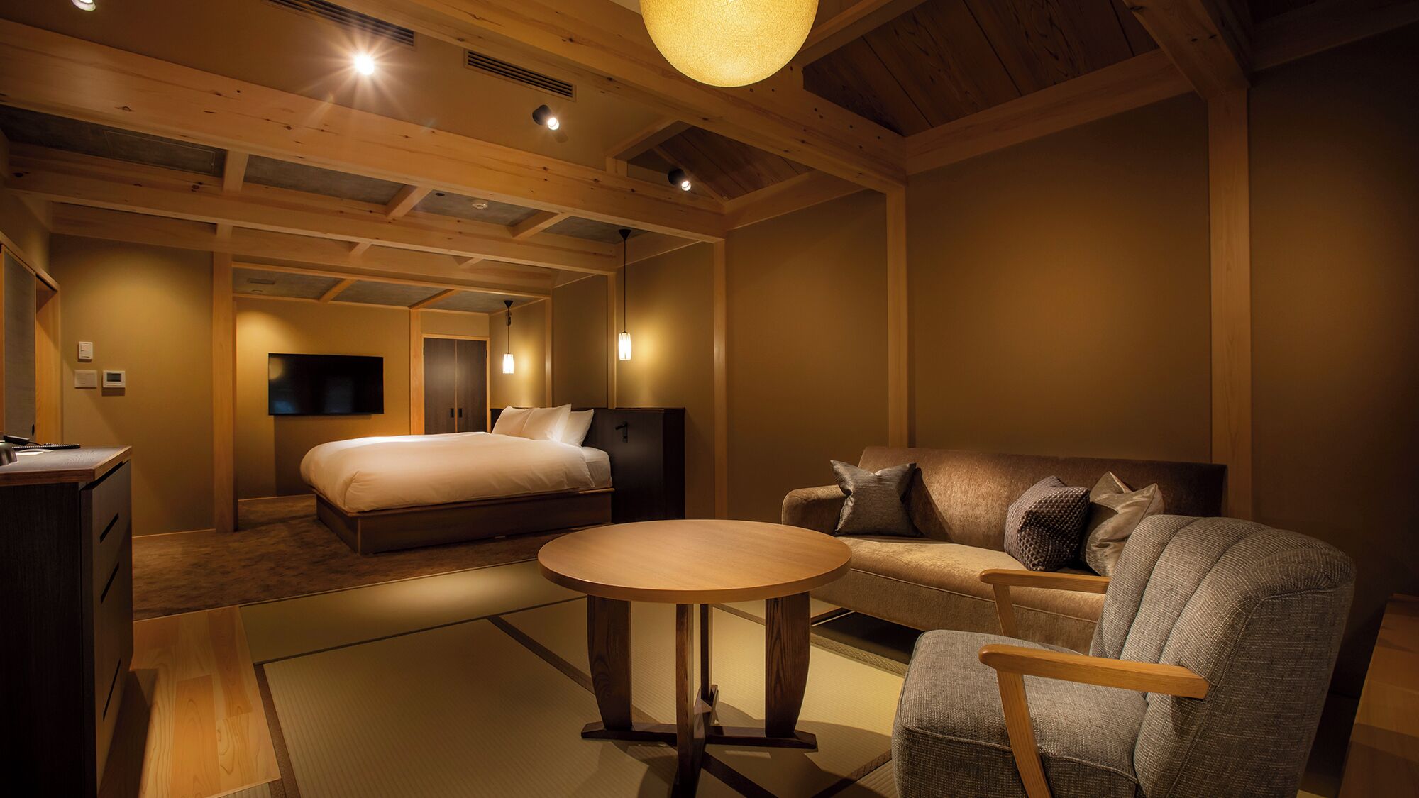 A hotel room with a bed, a sofa, a small table, and a TV.