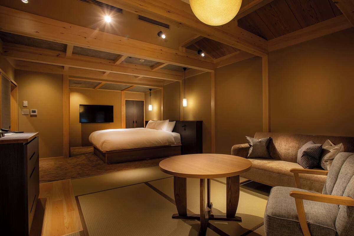 A hotel room with a bed, a sofa, a small table, and a TV.