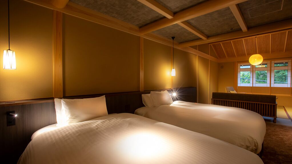 Habitación de hotel con dos camas, vigas de madera, una ventana con vistas e iluminación colgante.