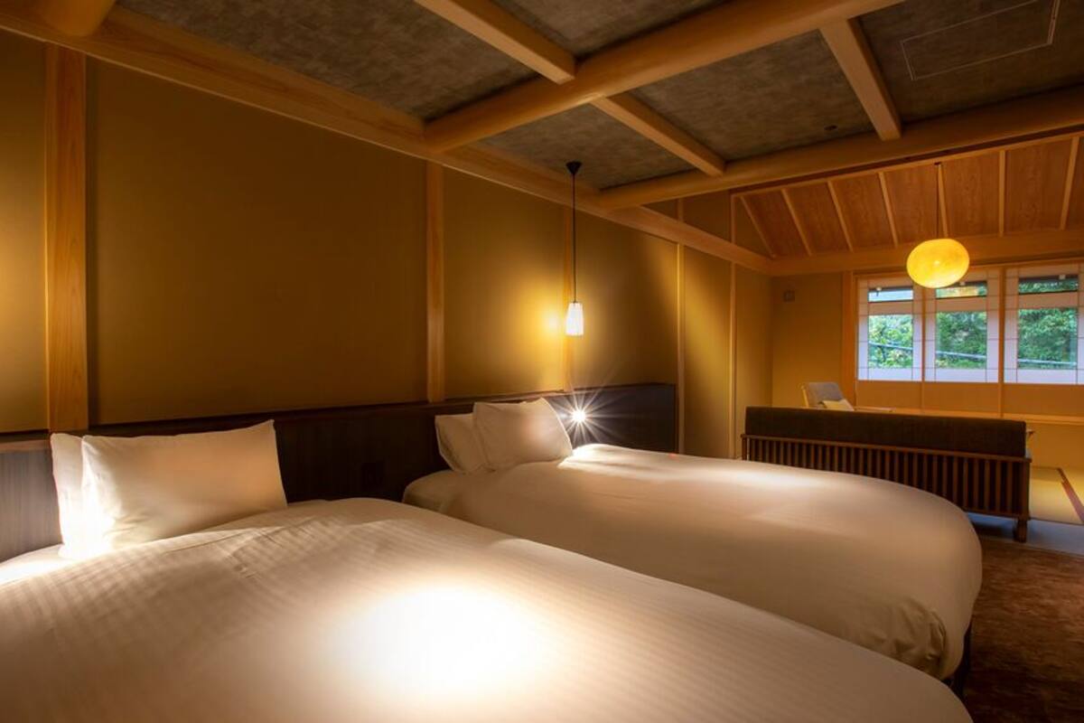 A hotel room with two beds, wooden beams, a window with a view, and pendant lighting.