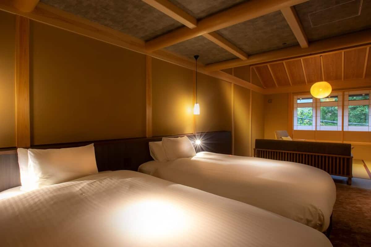 Habitación de hotel con dos camas, vigas de madera, una ventana con vistas e iluminación colgante.