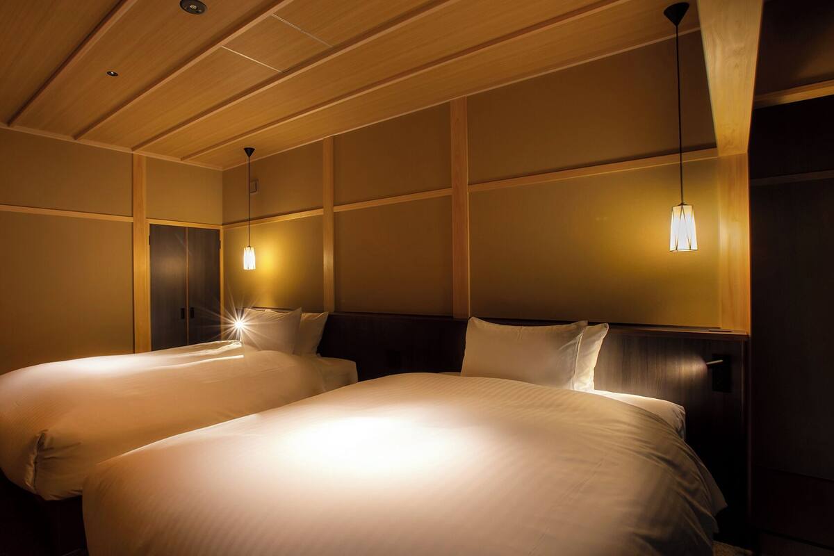 A hotel room with two beds, wooden paneling on the walls, and pendant lights.