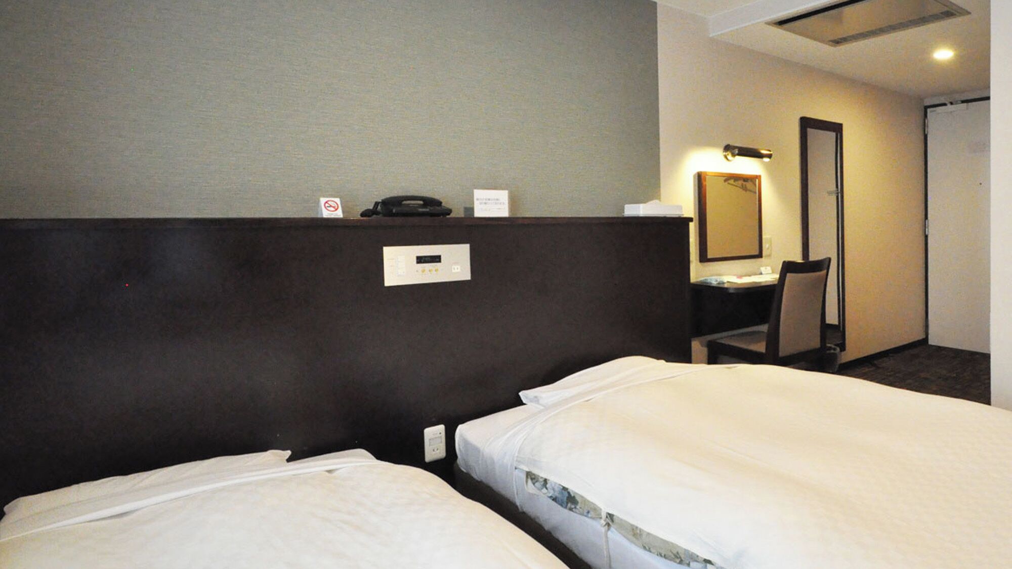 A hotel room with two beds, a desk, a chair, a mirror, and a door.