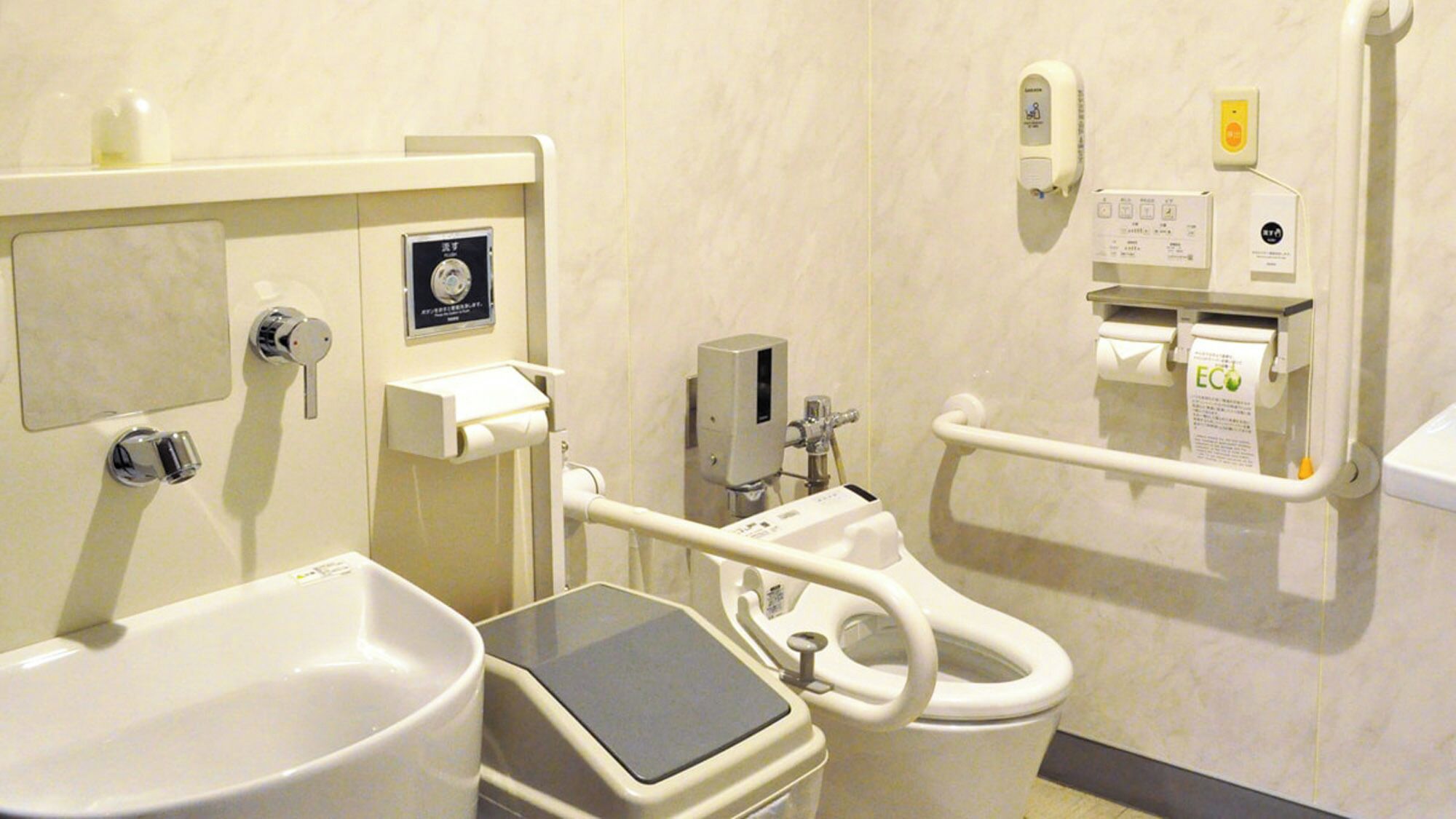 Un baño con inodoro, bidé, secamanos y dispensador de jabón.
