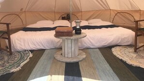 A tent with two beds, a central table with a lantern, and a patterned rug.