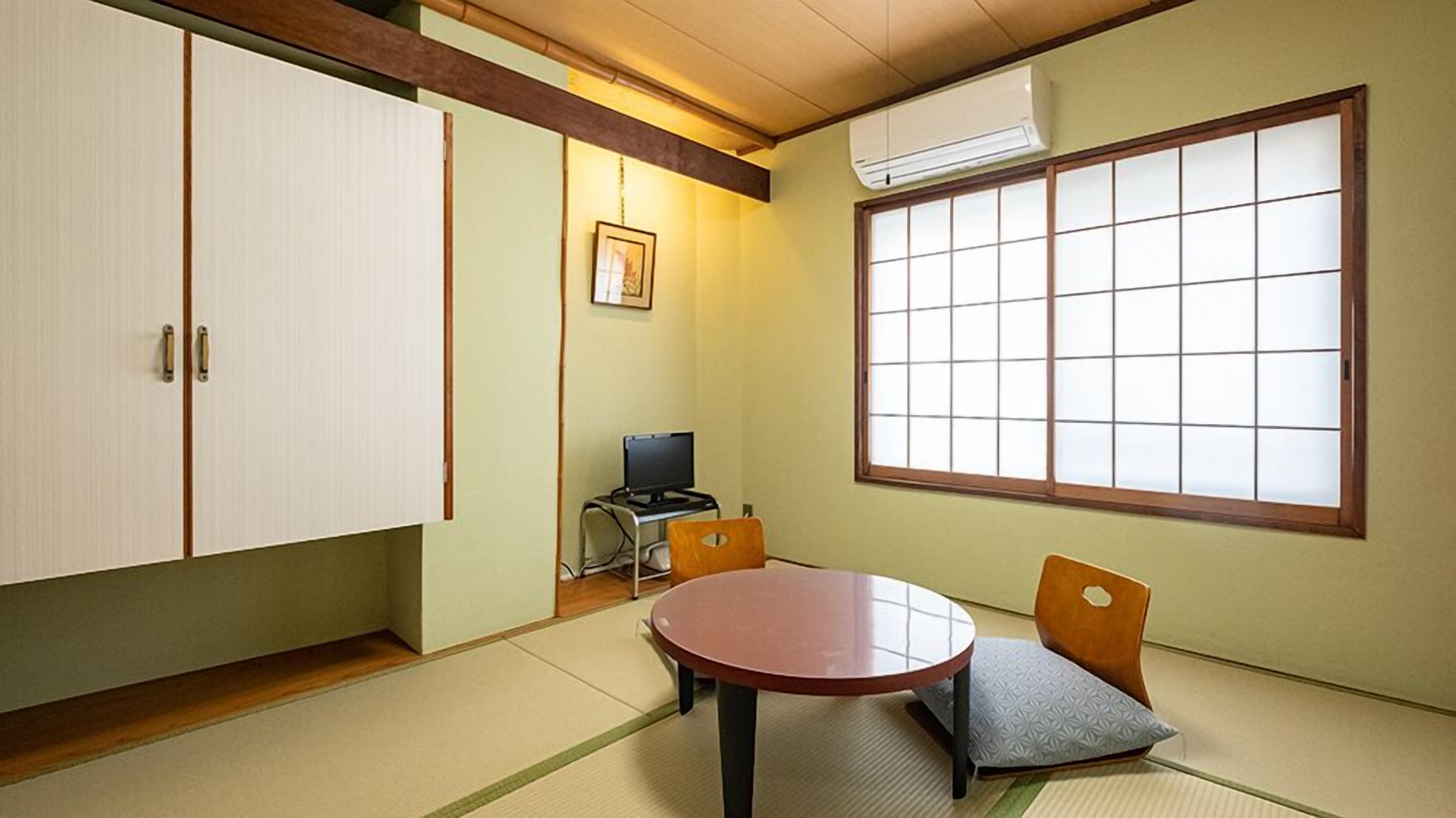 A traditional Japanese room with tatami flooring, a tatami mat table, a low wooden desk with a computer, a large shoji screen window, and a sliding door.