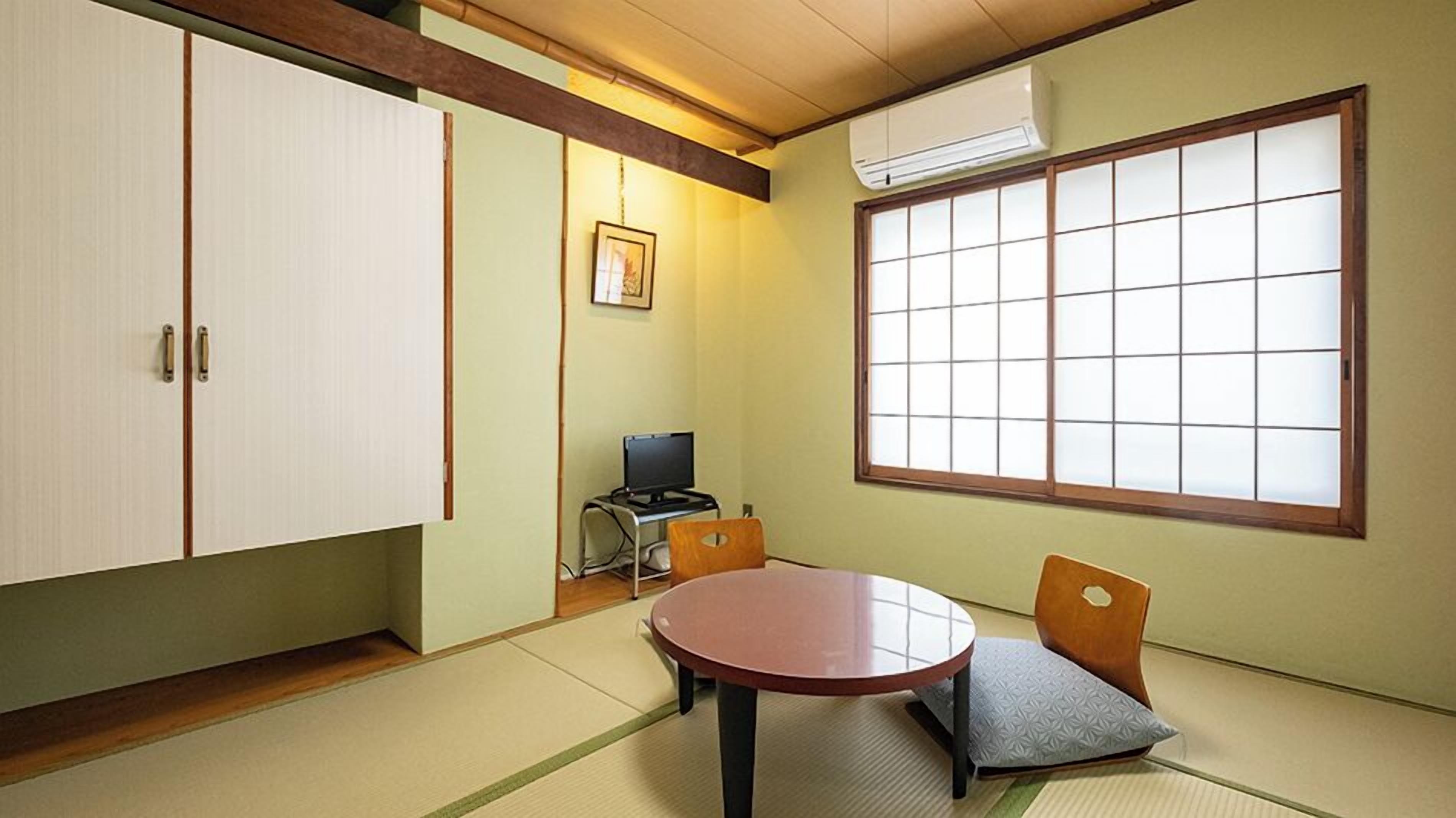 A traditional Japanese room with tatami flooring, a tatami mat table, a low wooden desk with a computer, and a large shoji screen window.