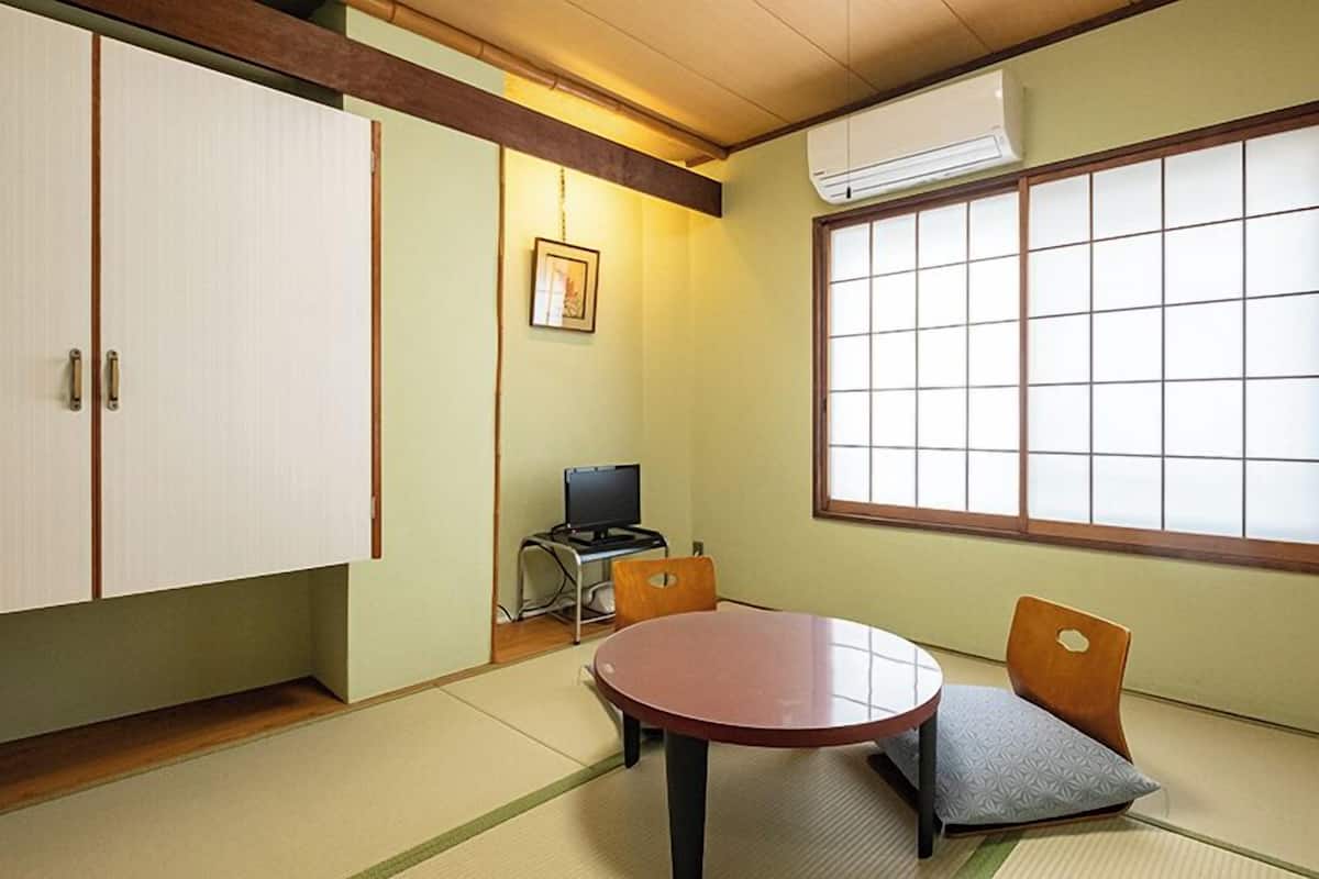 A traditional Japanese room with tatami flooring, a tatami mat table, a low wooden desk with a computer, and a large shoji screen window.