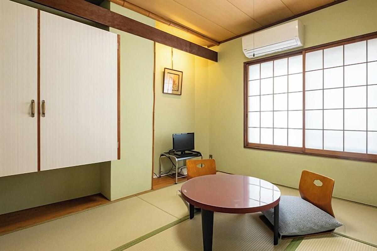 A traditional Japanese room with tatami flooring, a tatami mat table, a low wooden desk with a computer, and a large shoji screen window.