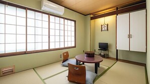 Een traditionele Japanse kamer met tatami vloeren, een lage tafel met kussens, een televisie en schuifdeuren.