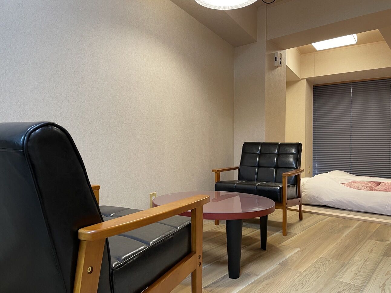 A room with a bed, two leather chairs, a small round table, and a ceiling light.