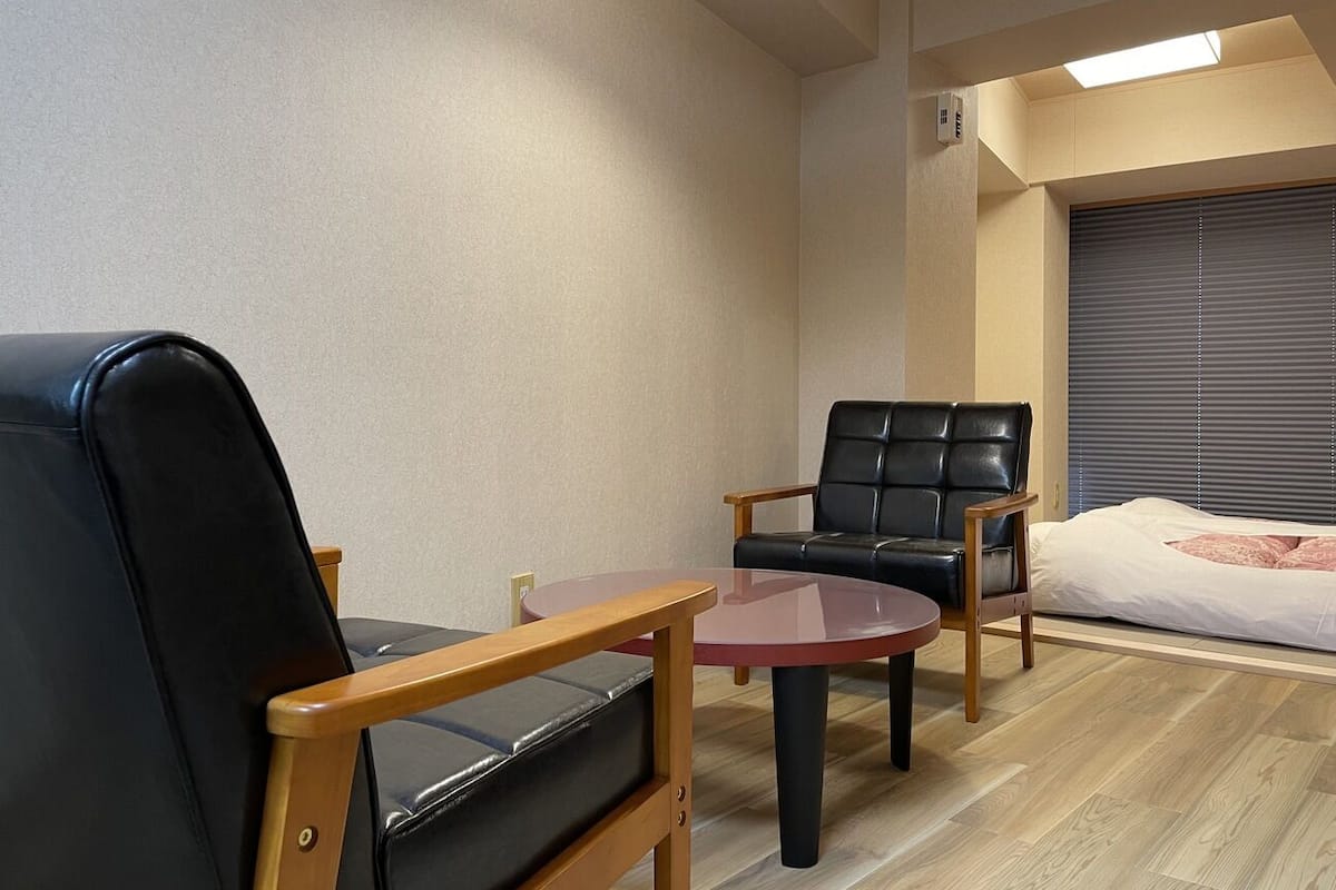 A room with a bed, two leather chairs, a small round table, and a ceiling light.