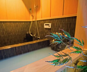 A bathroom with a wooden bench, a shower area, and a small plant on the counter. - Kyoran-ruantei (Kyoto)