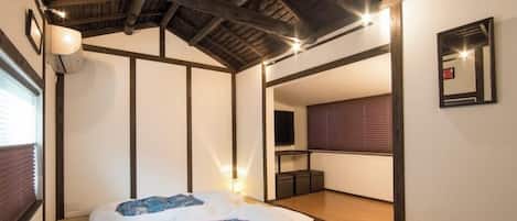 A bedroom with a bed, a bedside table, a mirror, and a window with blinds.