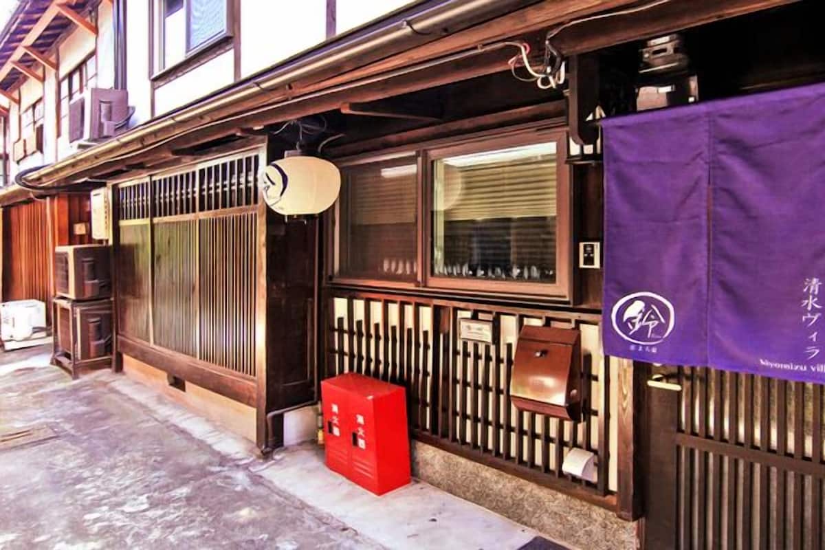 Ein traditionelles japanisches Gebäude mit Holzschiebetüren, einem roten Briefkasten und einem violetten Banner mit einem Logo.