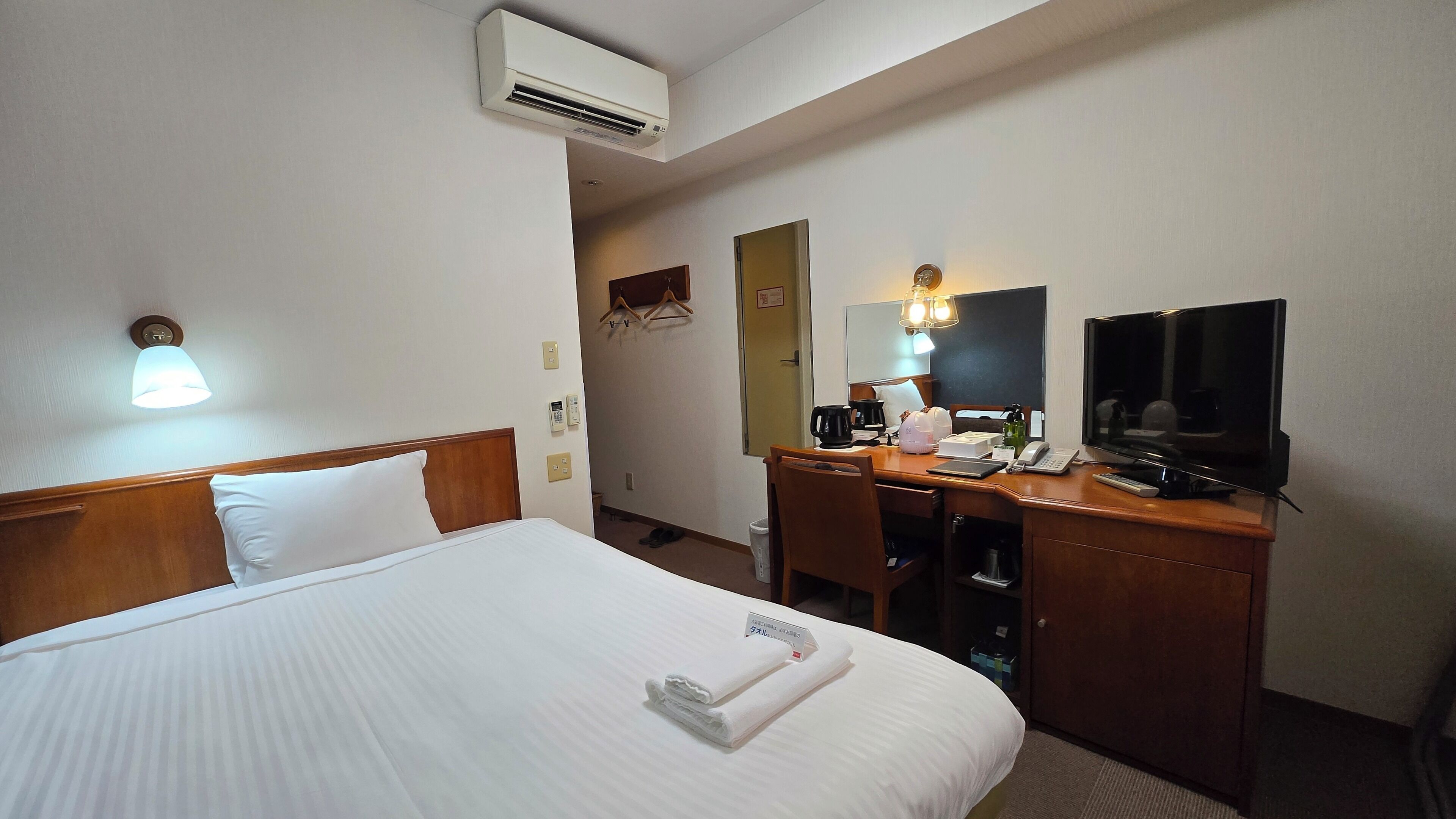 Ein Hotelzimmer mit Bett, Schreibtisch mit Stuhl, Fernseher und Spiegel.