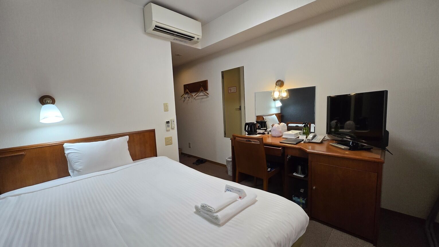 A hotel room with a bed, a desk, a television, and an air conditioning unit.