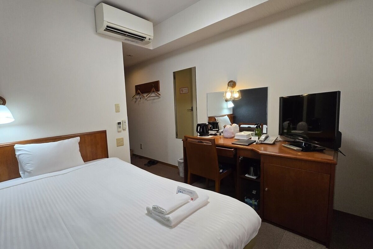 A hotel room with a bed, a desk, a television, and an air conditioning unit.