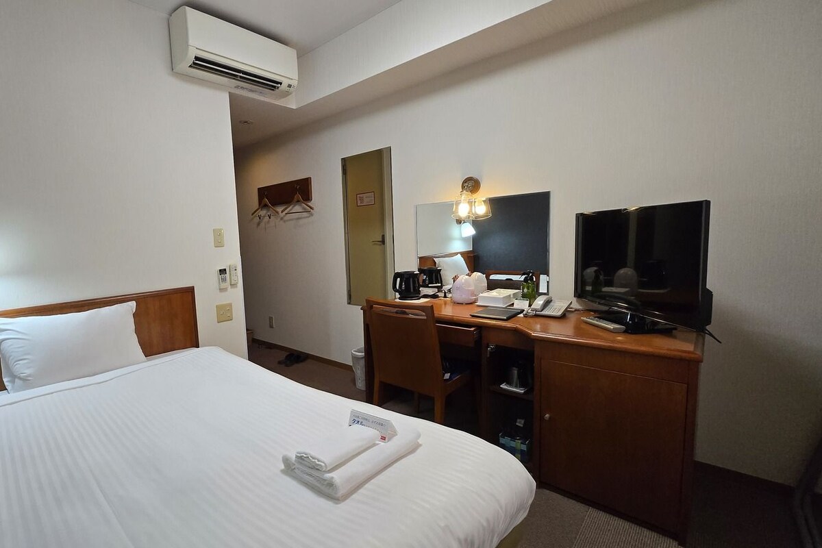 Quarto de hotel com cama, escrivaninha, televisão e ar condicionado.