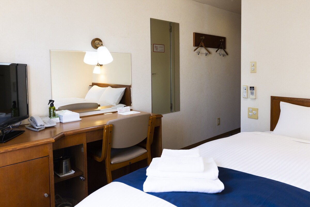 A hotel room with a bed, a desk with a telephone, a mirror, and a television.