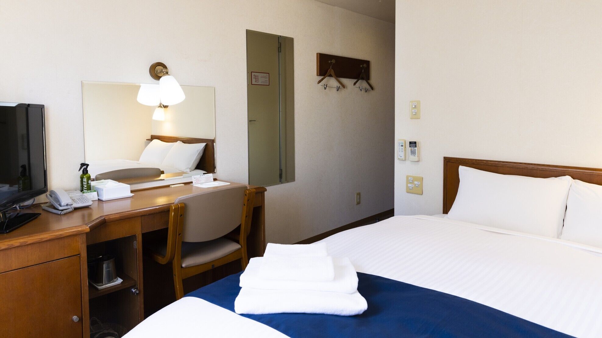 A hotel room with a bed, a desk with a lamp, a telephone, and a mirror.