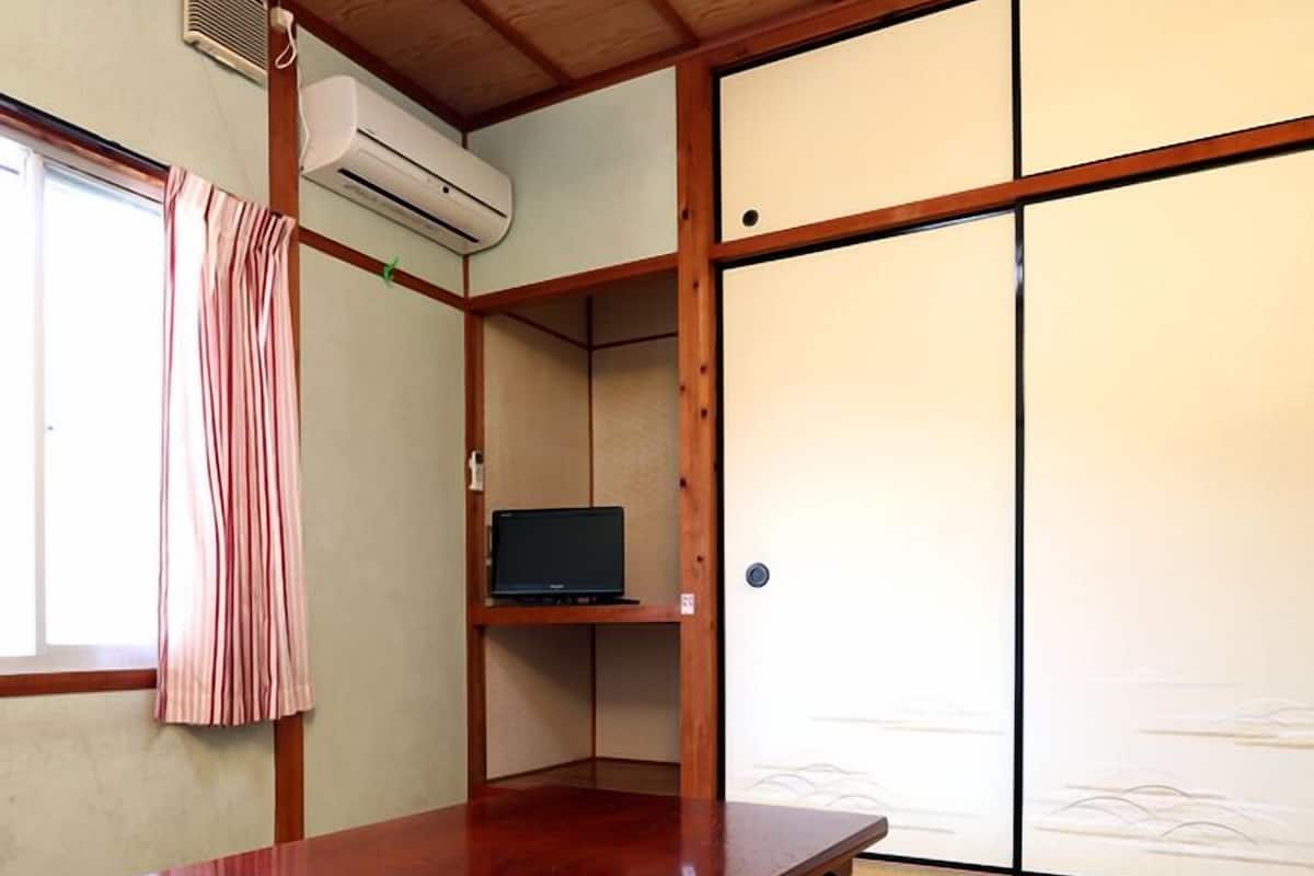 A traditional Japanese room with tatami flooring, a wooden table, a TV on a shelf, and sliding doors.
