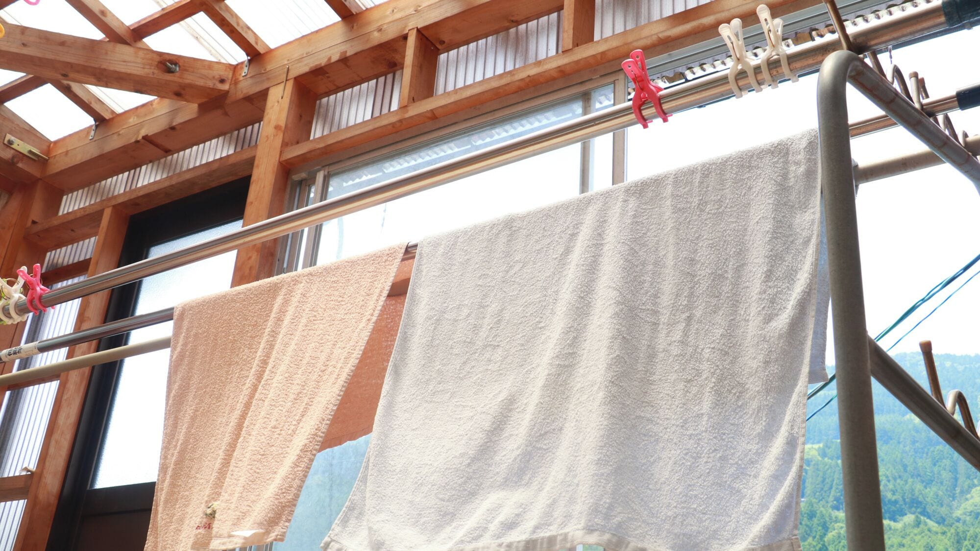 A room with a wooden ceiling, a window with a view of a forest, and two towels hanging on a rack.