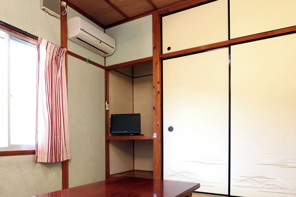 A traditional Japanese room with tatami flooring, a low wooden table, a television on a shelf, and sliding doors.