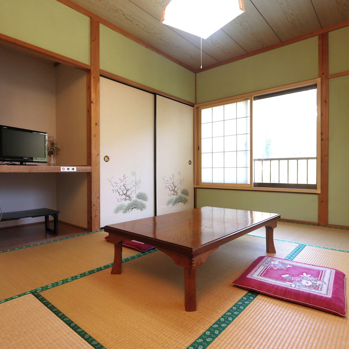 A traditional Japanese room with tatami flooring, a low wooden table, sliding doors with floral designs, and a television on a shelf.