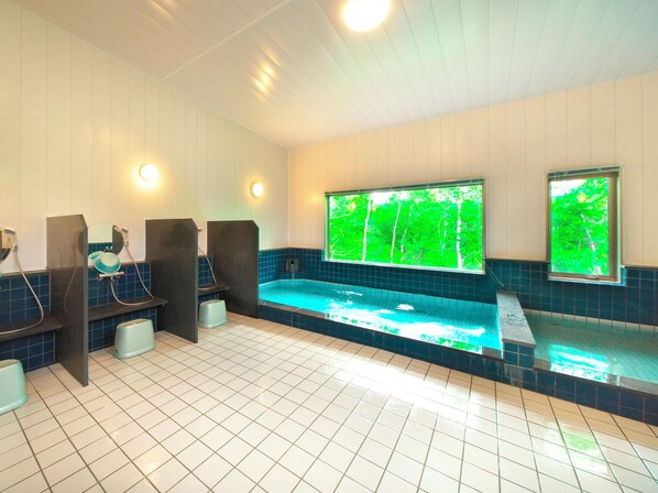 Un espace bien-être comprenant un jacuzzi, deux fenêtres donnant sur un paysage verdoyant et un sol carrelé.