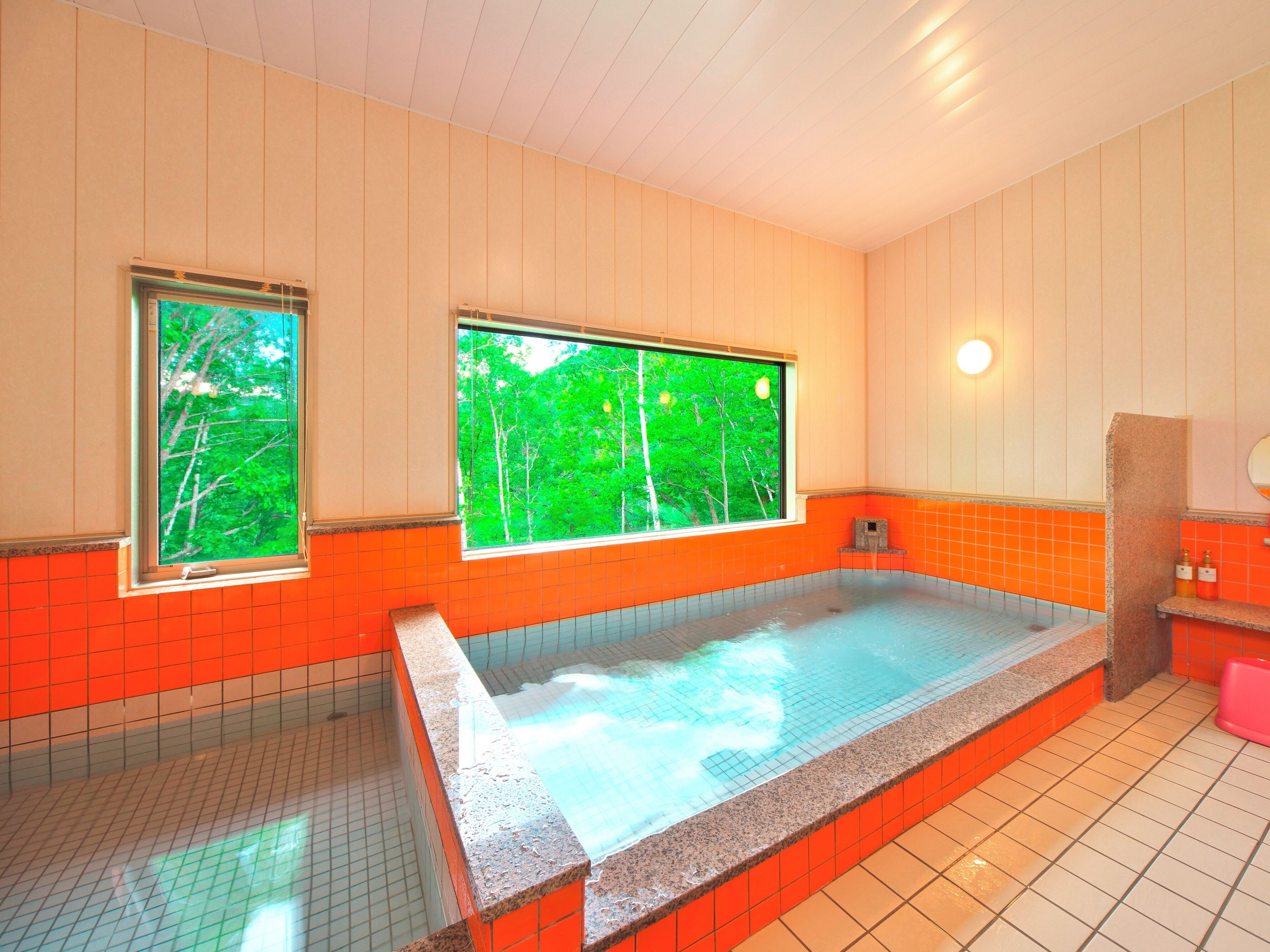 A spa room with a large bathtub, two windows with a view of trees, and orange tiled walls.